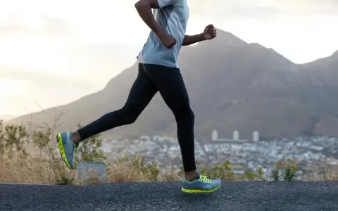 Un homme en tenue de sport fait du cardio training en courant sur une route de montagne, avec une ville en contrebas et des montagnes en arrière-plan.