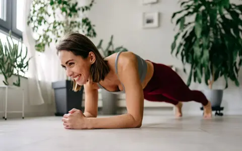 Femme souriante en position de gainage, profitant de son entraînement quotidien à domicile.