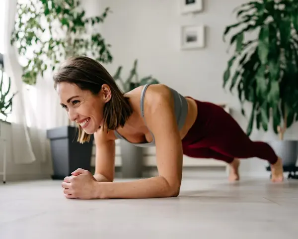 Femme souriante en position de gainage, profitant de son entraînement quotidien à domicile.