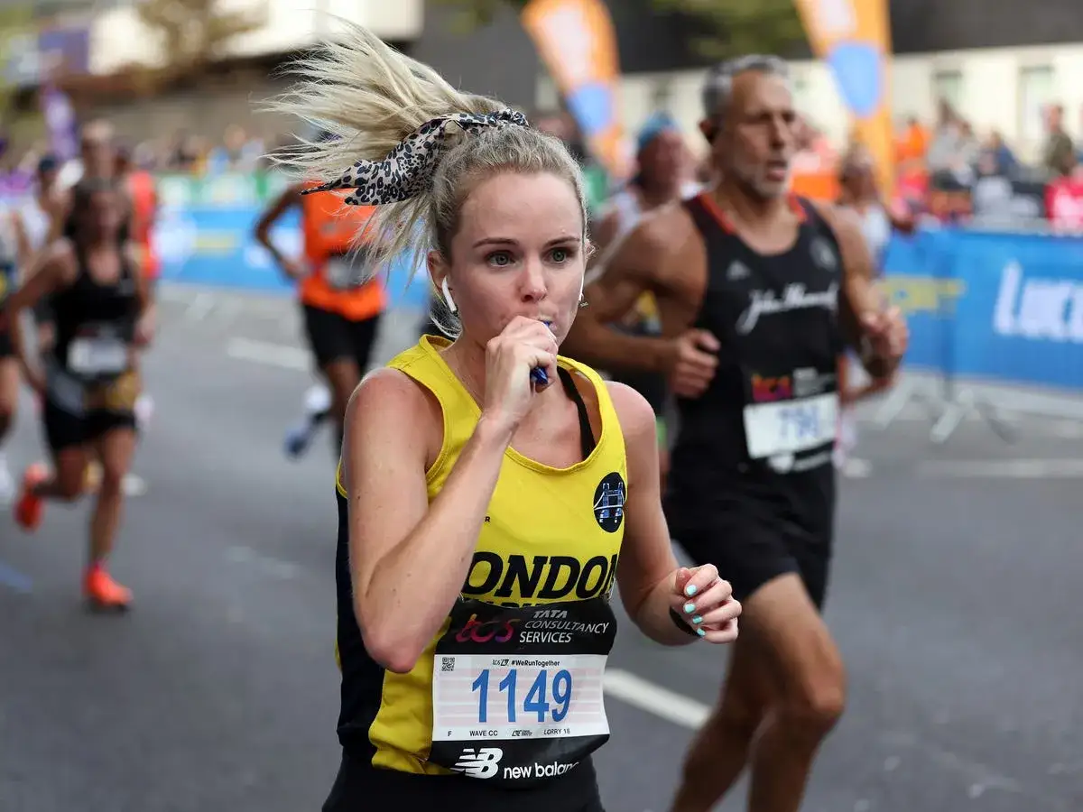 Coureuse de semi-marathon prenant un gel énergétique, crucial pour la nutrition pendant l'effort. Cheveux blonds en queue de cheval, dossard 1149.