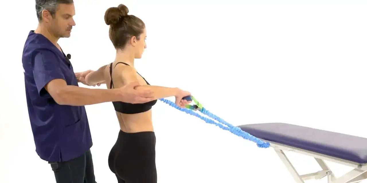 Un kinésithérapeute guide une femme dans des exercices de tendinite épaule avec un élastique.