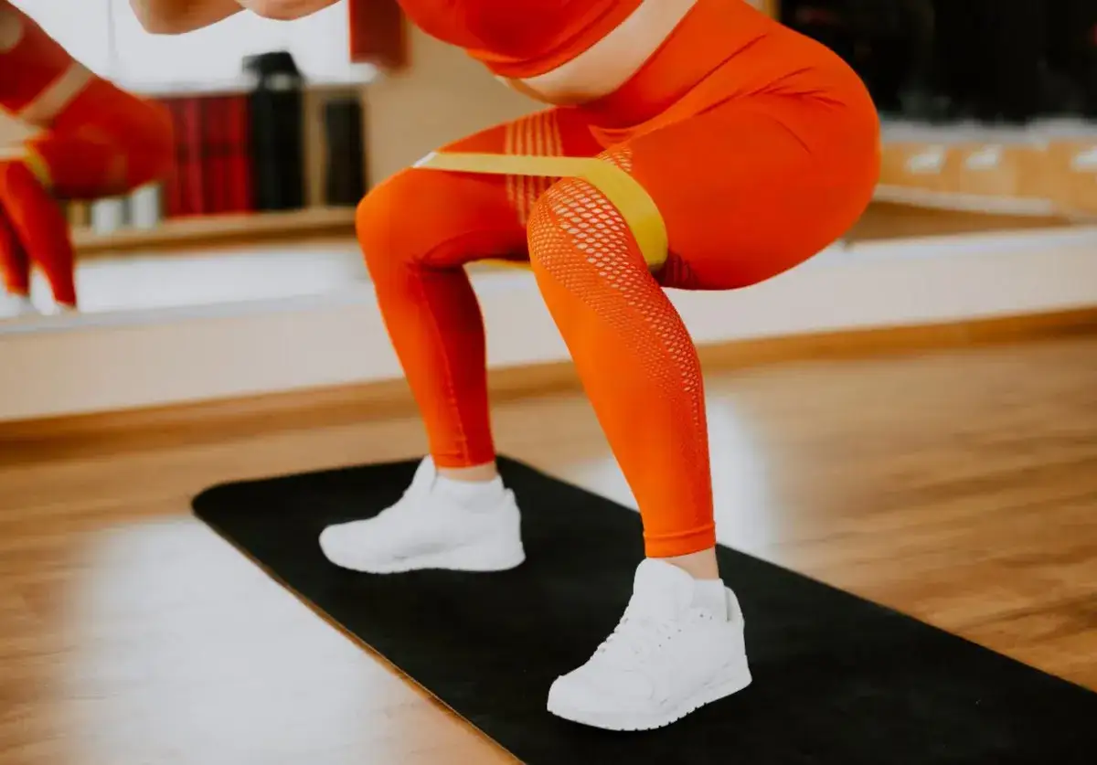 Femme en tenue orange faisant un squat avec une bande de résistance autour des cuisses.