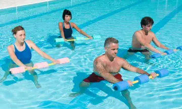 Quatre personnes font un exercice piscine avec des haltères flottants. L'eau bleue reflète la lumière du soleil.