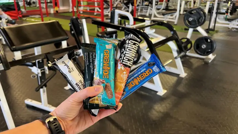 Une main tient plusieurs barres protéinées, parfaites comme collation avant ou après le sport, dans une salle de sport.